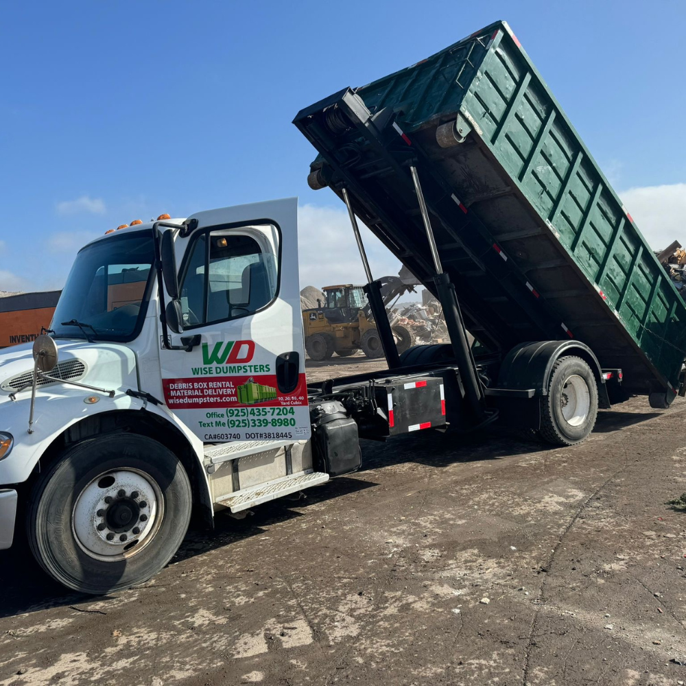 Wise Dumpsters truck unloading a green roll-off against a blue sky